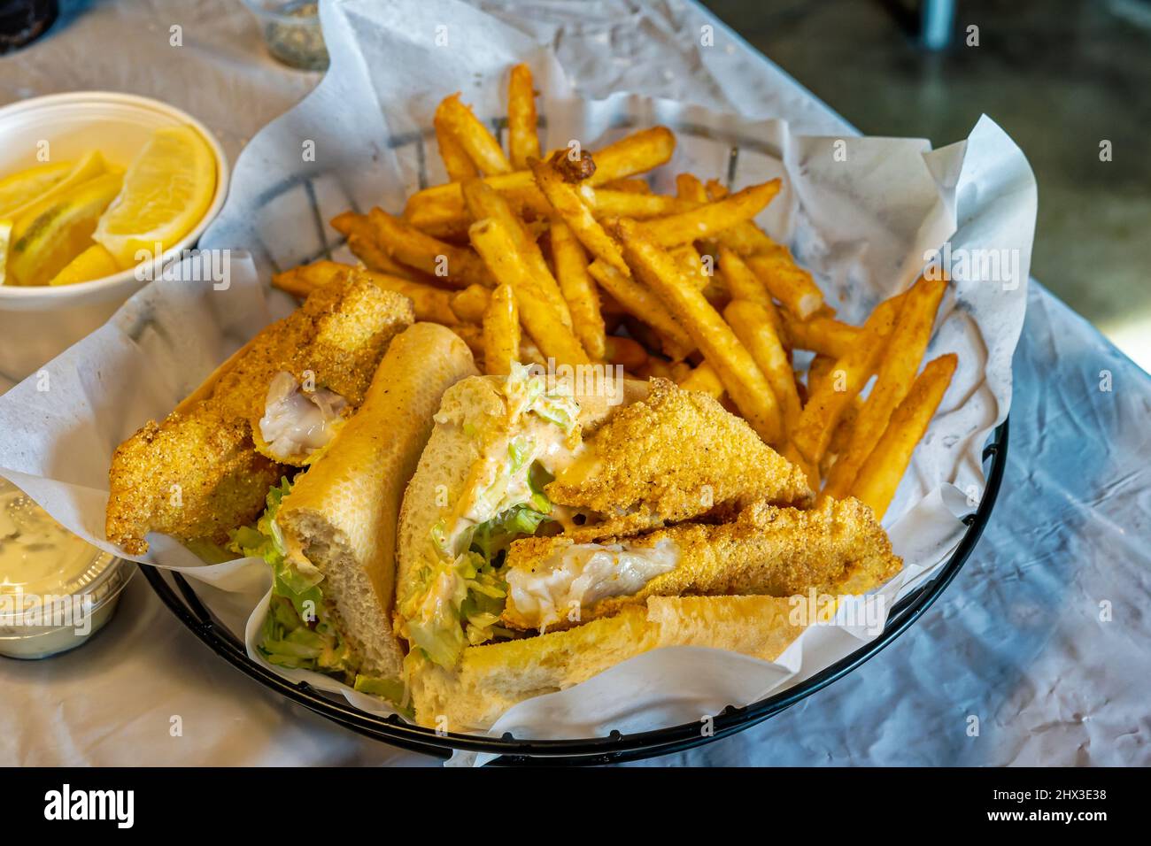 Cajun pesce gatto po ragazzo sandwich in un cestino con patatine fritte e una tazza di spicchi di limone accanto Foto Stock