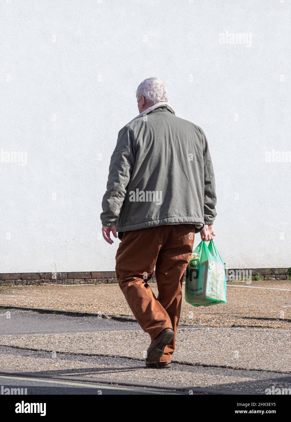 Uomo anziano che si riparte dal negozio o dal negozio con una borsa in plastica per il trasporto di un supermercato Co-op, Regno Unito Foto Stock