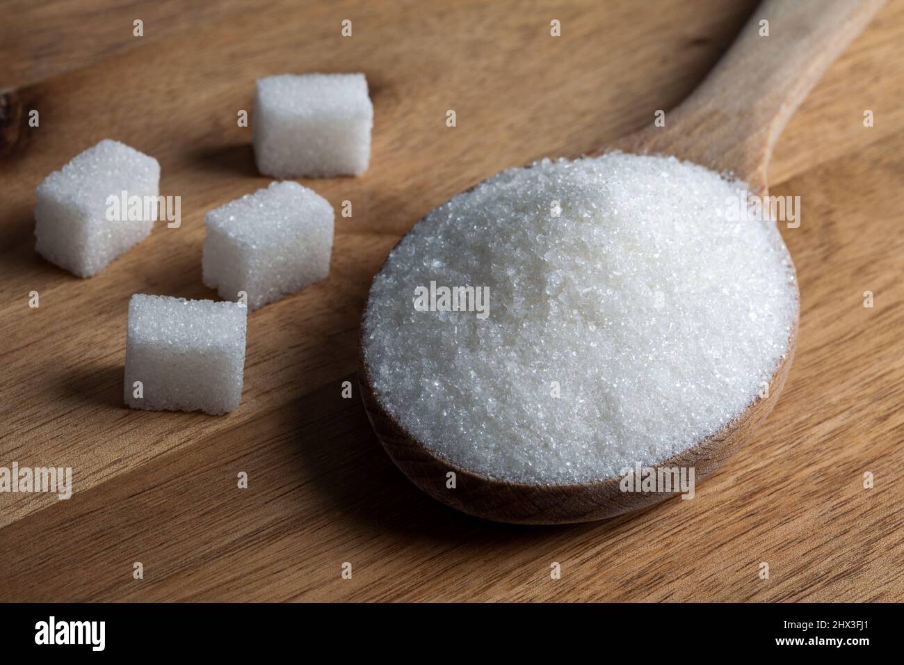 Zucchero granulato e cubetti di zucchero in cucchiaio di legno su sfondo di legno Foto Stock