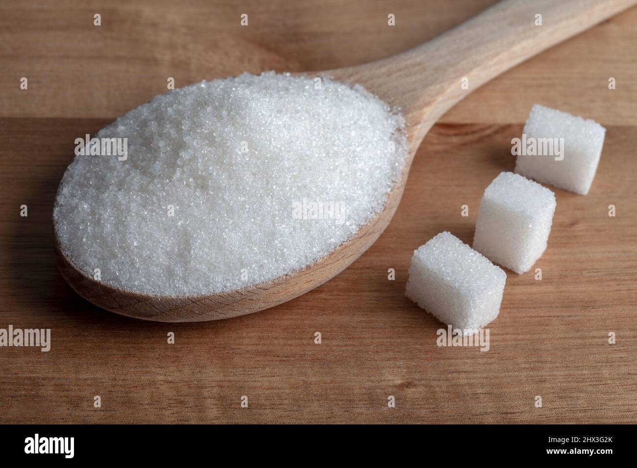 Zucchero granulato e cubetti di zucchero in cucchiaio di legno su sfondo di legno Foto Stock