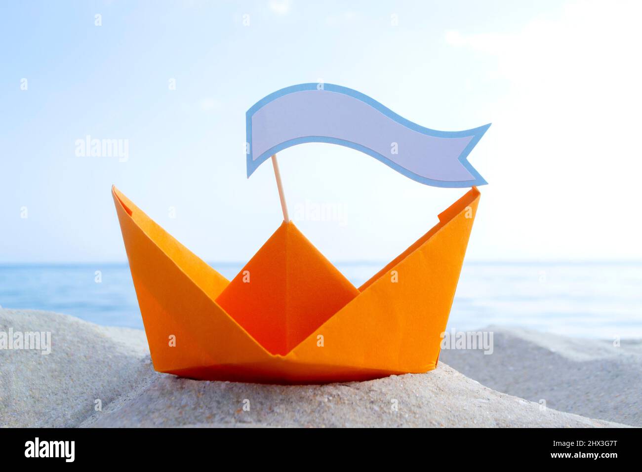 Orange Paper Boat su Sandy Seashore primo piano piccola barca da carta su sfondo Foto Stock