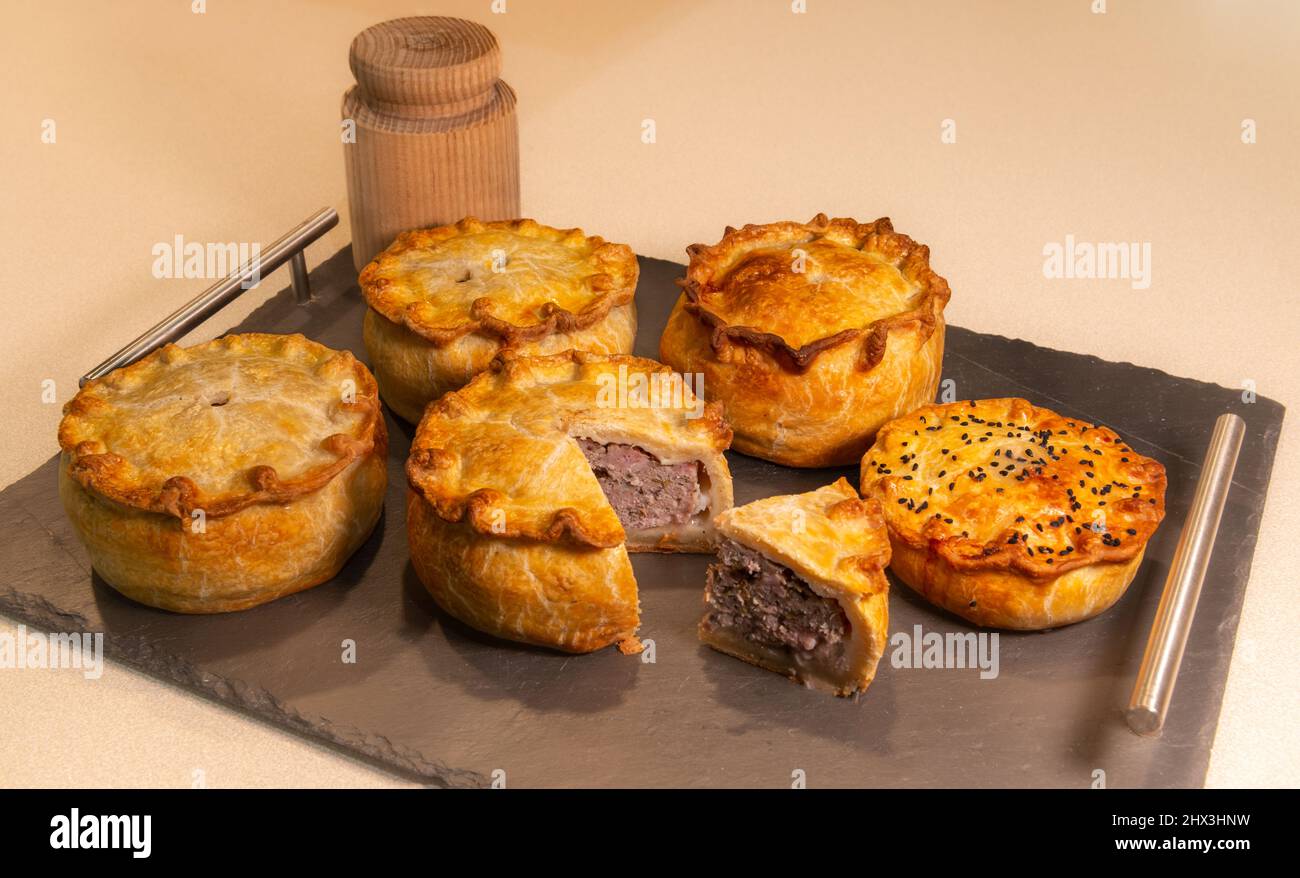 Un vassoio con cinque deliziose torte di maiale rialzate a mano e cotte insieme a un tradizionale dolce torta utilizzato per la loro produzione Foto Stock