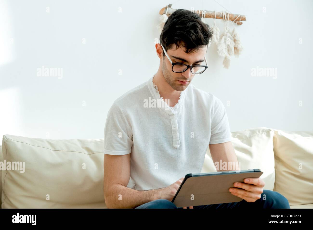 Ritratto di un freelance maschile che è sempre in contatto a casa. Bell'uomo ha messo a fuoco il suo smartphone mentre si siede sul divano. Foto Stock