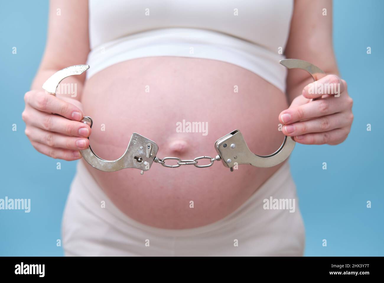 Manette nelle mani di una donna incinta, foto studio su sfondo blu Foto Stock