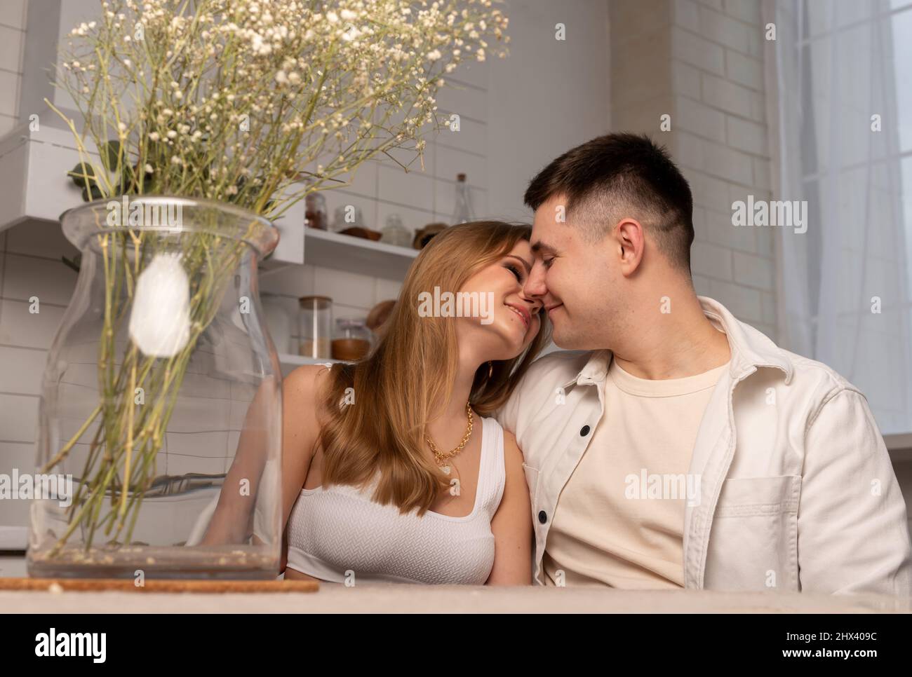 Coppia felice seduta al tavolo da cucina, baciando delicatamente e guardandosi l'un l'altro. Concetto di amore e romanticismo. Foto di alta qualità Foto Stock