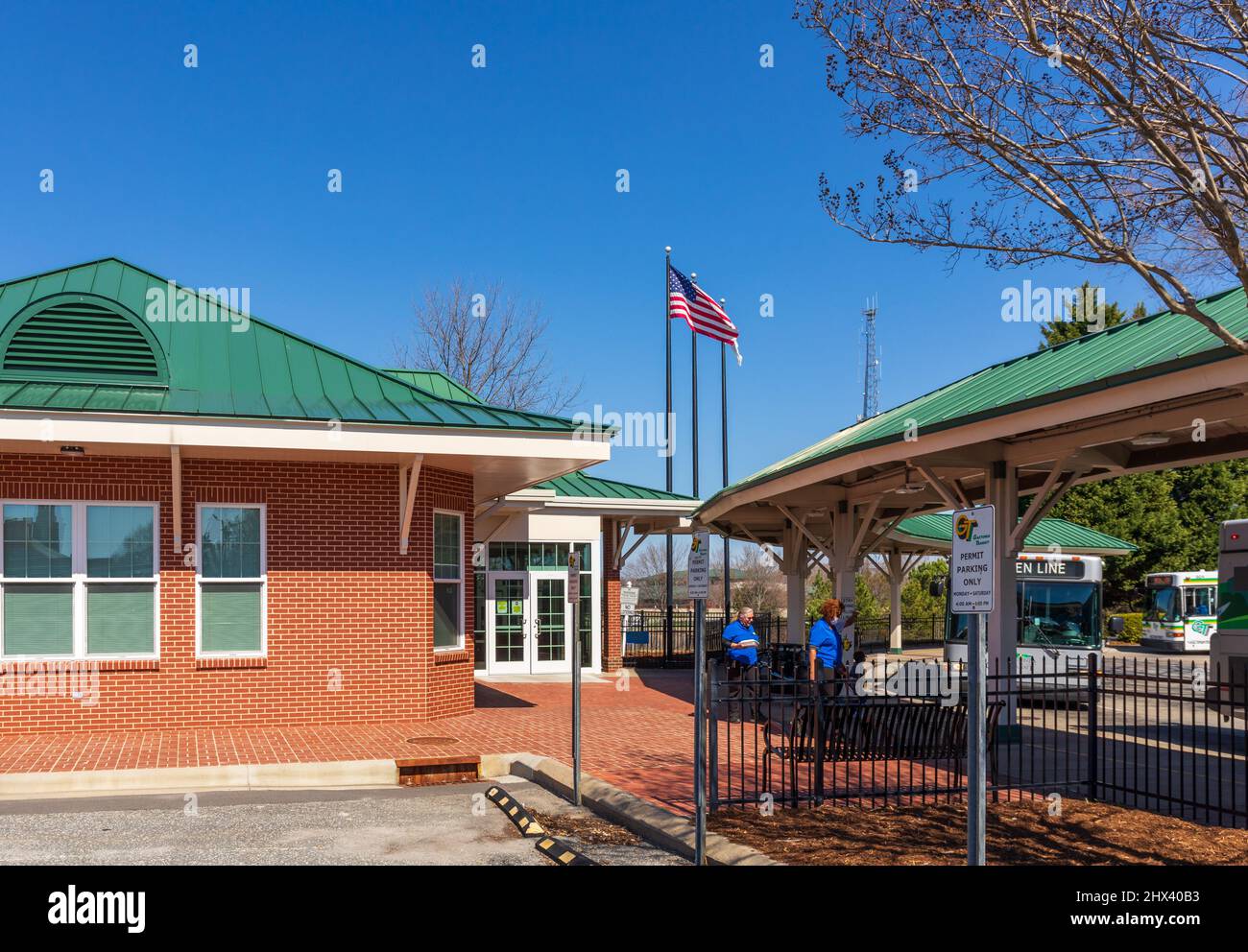 GASTONIA, NC, USA-3 MARZO 2022: Edificio del terminal degli autobus urbani, con due autisti a piedi per i loro autobus. Autobus in linea e pali di bandiera. Foto Stock