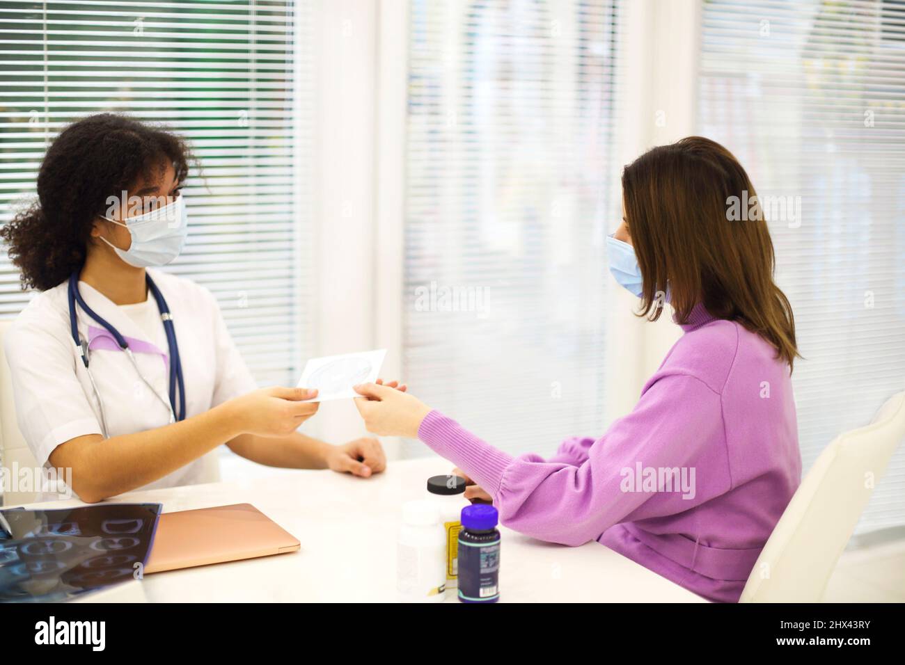 Medico afro-americano donna indossare maschera facciale dando CD con immagine a raggi X a paziente durante appuntamento medico in clinica o ospedale, selecti Foto Stock