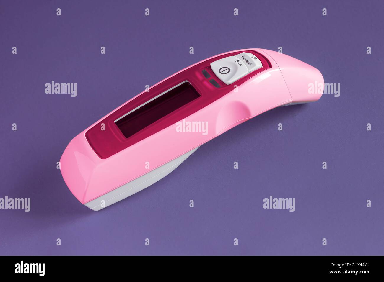 Termometro rosa laser per orecchie e fronte per famiglie su sfondo colorato dello studio. Medicina e tecnologia. Foto Stock