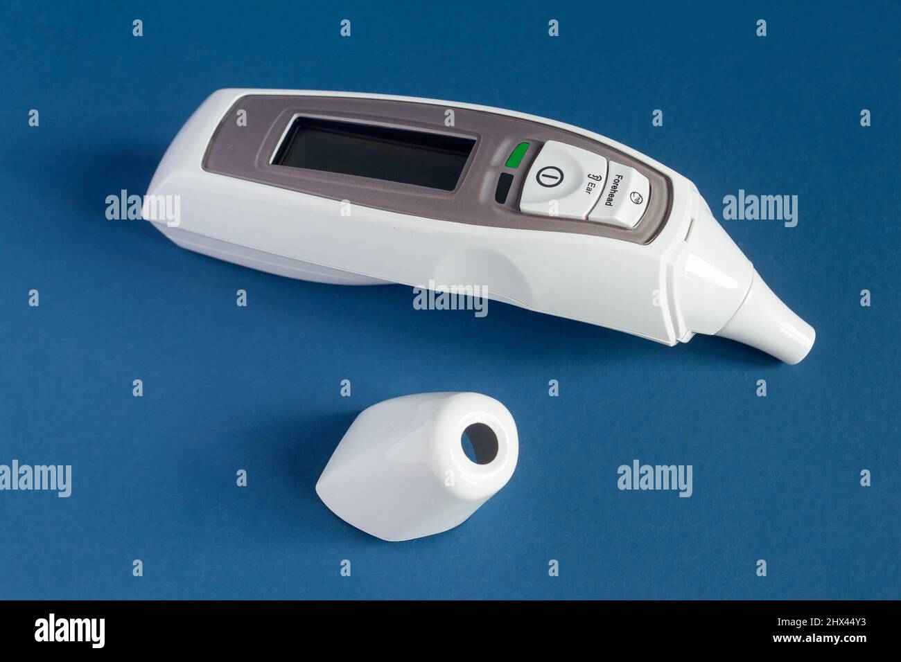 Termometro a infrarossi per fronte e orecchio con display LCD e allarme febbre con tappo rimosso su sfondo blu-pastello. Assistenza sanitaria e Foto Stock