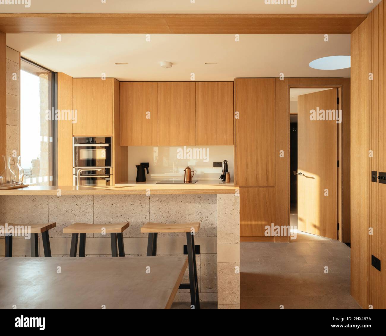 Vista interna della calda cucina in pannelli di legno e del bar per la colazione. Clifftops, Dorset, Portland, Regno Unito. Architetto: Morrow + Lorraine Architetti, 2 Foto Stock