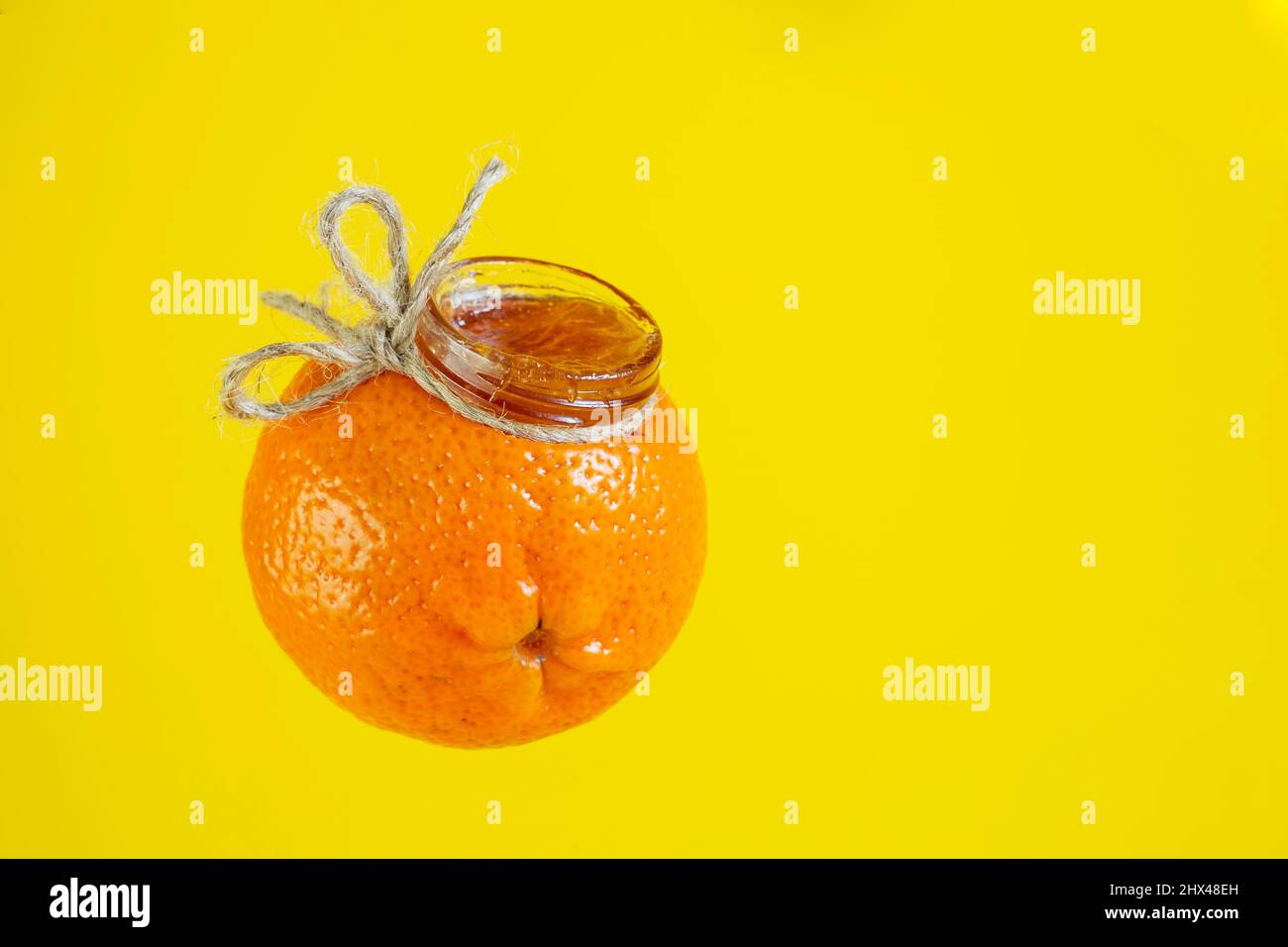 Marmellata di marmellata in un vaso con la forma di un mandarino arancione isolato su giallo Foto Stock