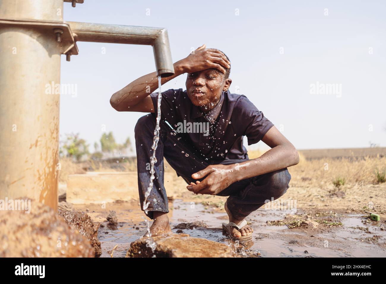 Giovane ragazzo africano esaurito villaggio rinfrescare la sua fronte al punto d'acqua pubblico in un deserto subsaharian secco area; la consapevolezza globale del clima ch Foto Stock