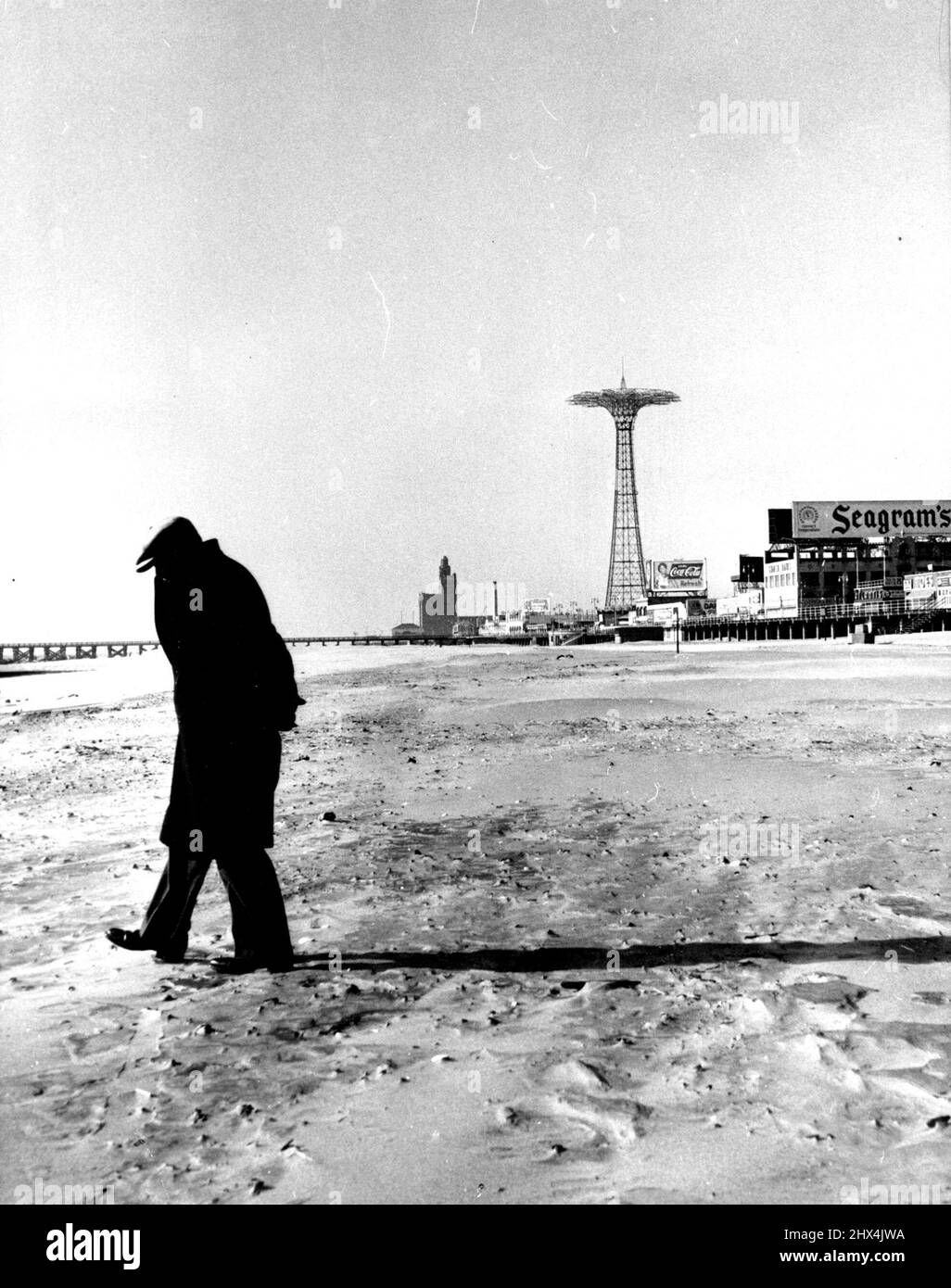 Questo passeggino solitario si snoda lungo la spiaggia della famosa Coney Island, alla ricerca di monete, anelli e altri oggetti di valore persi durante l'estate. I freddi venti di dicembre scacciano la riva, disturbando un mondo altrimenti tranquillo. La torre di "paracadute jump" si infila sullo sfondo, una sentinella muta sul luogo desolato d'inverno. Agosto 12, 1955. (Foto di United Press Photo). Foto Stock