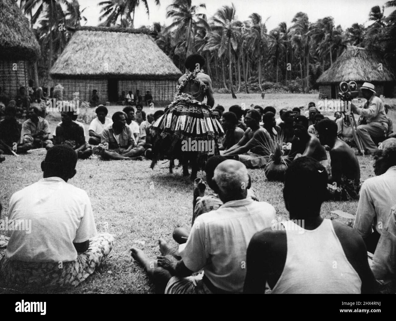 Fiji darà il benvenuto alla Regina. Durante la sua visita alle Figi la Regina guarderà un certo numero di attività cerimoniali. Qui i Fiji ricevono Kava, la bevanda nazionale, fatta dalla radice secca di una pianta appartenente alla famiglia del pepe. La produzione e il servizio del kava è un lavoro per i giovani uomini. Qui uno degli assistenti di Kava, vestito in abito cerimoniale di corteccia-stoffa e giardini di fiori, consegna tazze di kava agli ospiti seduti. Dicembre 2, 1953. (Foto di Paul Popper). Foto Stock