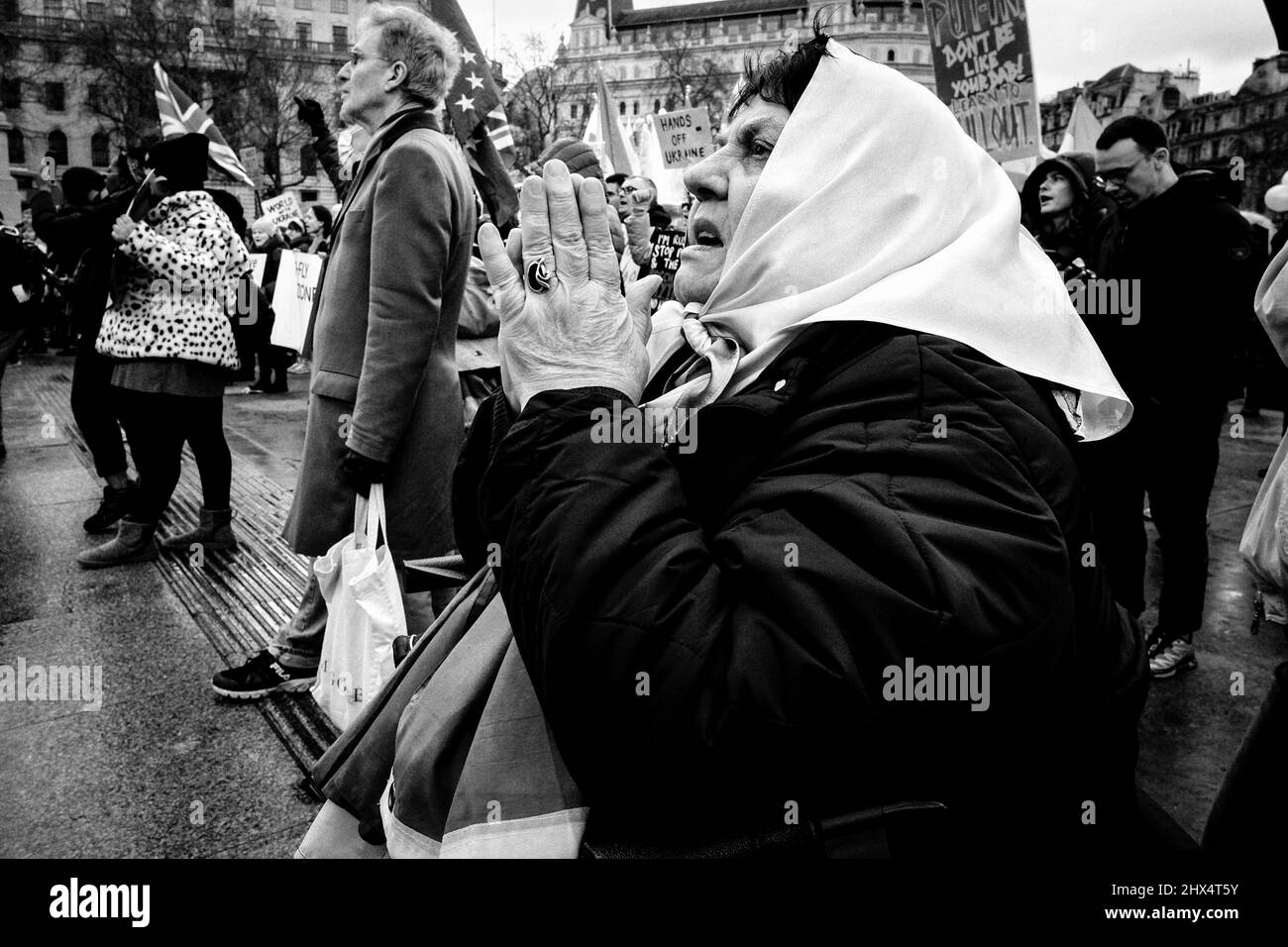 Una donna anziana drapponata alla bandiera Ucraina tiene le mani insieme in preghiera alla manifestazione anti-guerra in piazza Trafalgar. Foto Stock