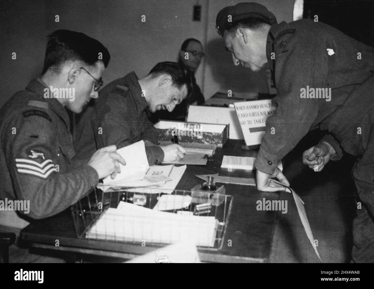 Primo giorno di 'demob' -- la routine di demob. Gli impiegati stanno controllando le carte di Gunner George Allfree, mentre lui guarda sopra. La storia in immagini della smobilitazione di Gunner George Allfree di Walworth. All'età di 51 anni, era un gunner la scorsa guerra, un commissario, un gunner territoriale questa guerra, e sarà di nuovo un commissario. Servì in una brigata A.A. nell'estuario del Tamigi. Giugno 18, 1945. Foto Stock