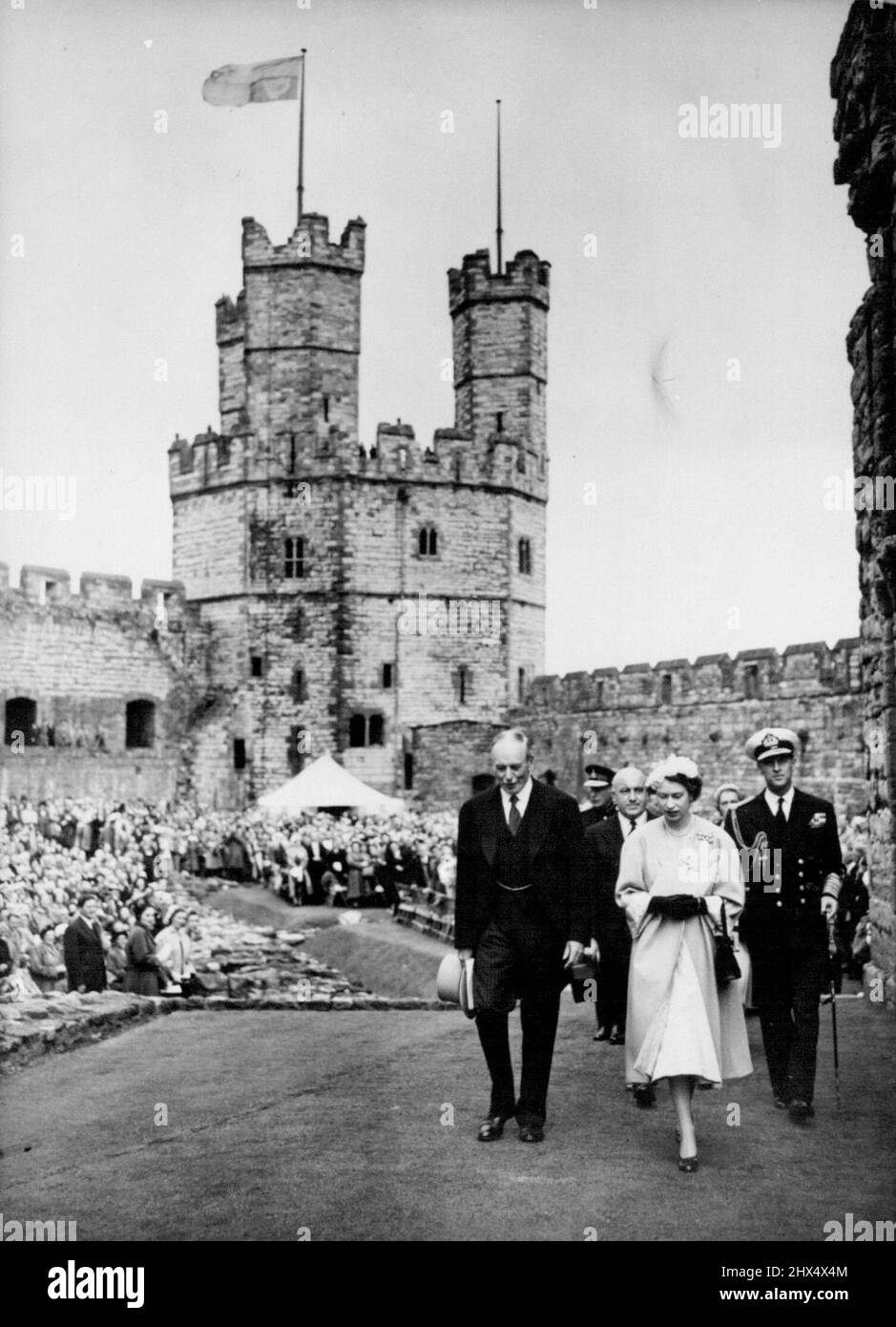 Regina e Duca Visita il Castello di Caernarvon -- la Regina Elisabetta II e il Duca di Edimburgo (destra), accompagnati da Lord Harlech, constabile del castello di caernarvon (sinistra), sono seguiti da Sir David Maxwell Fyfe, il segretario di casa mentre camminano attraverso i giardini del castello, luglio 10th. Lo standard reale vola dalla torre del castello. Quarantamila persone hanno dato il benvenuto alla Regina quando ha visitato l'antico castello di Caernarvon oggi 10th luglio - la prima regnante regina ad entrare nella roccaforte gallese da quando il re Edoardo i l'ha costruita sette secoli fa. Su un balcone sopra la porta della regina Eleonora venne la regina Foto Stock