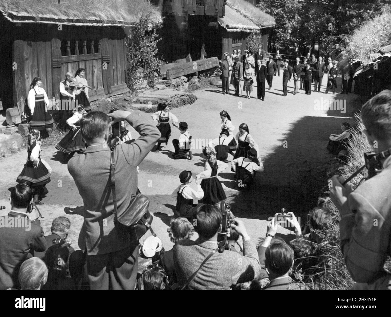 Visita reale in Norvegia -- un gruppo di bambini piccoli ***** Costumi della valle di Setes facendo un ***** Danzare nel cortile delle case coloniche del Medioevo al Museo Folcloristico Norvegese in onore della Regina. (Visto in background con il suo entourage. Il 24th giugno la Regina Elisabetta II e il Duca di Edimburgo arrivarono ad Oslo in una visita statale di 3 giorni in Norvegia. Questa è la prima visita della Regina in qualsiasi paese al di fuori del Commonwealth britannico. Il secondo giorno della visita includeva una festa in giardino presso l'Ambasciata britannica e uno spettacolo reale di Galla al Teatro Nazionale in serata. Giugno 25, 1955. Foto Stock