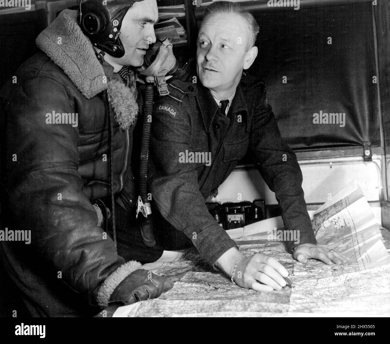 Uno squadrone della città di Oshawa Spitfire pilota, P/o Gord Cameron di Edmonton, è interrogato dopo una recce armata in territorio tedesco dal ufficiale di Duty Intelligence, F/L Alan MacNab di Toronto. I punti esatti in cui i piloti hanno incontrato il flak nemico, ha girato-up il trasporto tedesco o 'clobbered' un combattente Luftwaffe, sono contrassegnati sulla mappa da D.I.O. nel suo angolo del 'Int/Ops' Office-on-whees. Marzo 13, 1945. (Foto di RCAF Photo). Foto Stock