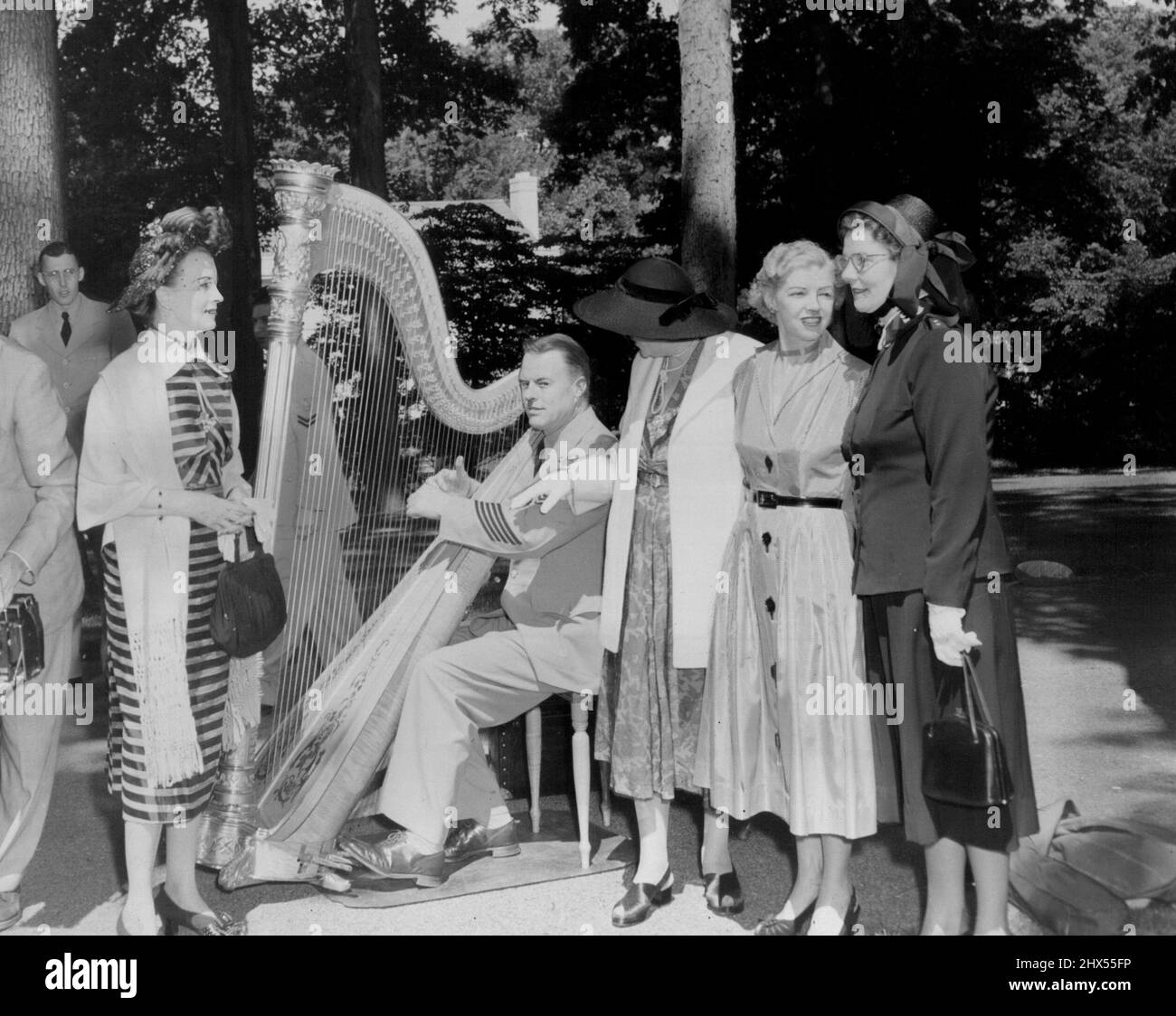 "rs. Walter Bedell Smith chiacchierò con l'arpista, il musicista capo William Cameron della United States Navy Band, che suonò nei giardini durante tutto il pomeriggio. La sig.ra Francis G. Ulen, presidente dell'Armata della salvezza ausiliaria, è sulla sinistra. In piedi con la sig.ra Bedell Smith sono Lady Spender e la sig.ra Brigadier William Range. Lady Spender e i suoi amici complimentano l'arpista Chief Musician William Cameron della US Navy Band per l'eccellente musica durante la festa. Giugno 29, 1953. Foto Stock