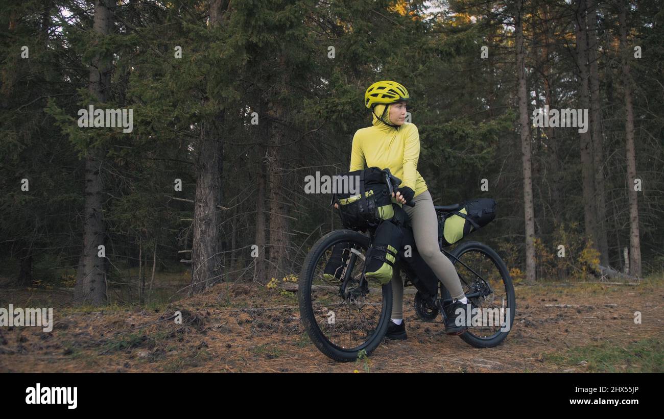 La donna viaggia in bicicletta su terreni misti con bikepacking in  bicicletta all'aperto. Il viaggio del viaggiatore con le borse della  bicicletta. Bikepacking elegante, bici, abbigliamento sportivo in verde  nero. Parco magico