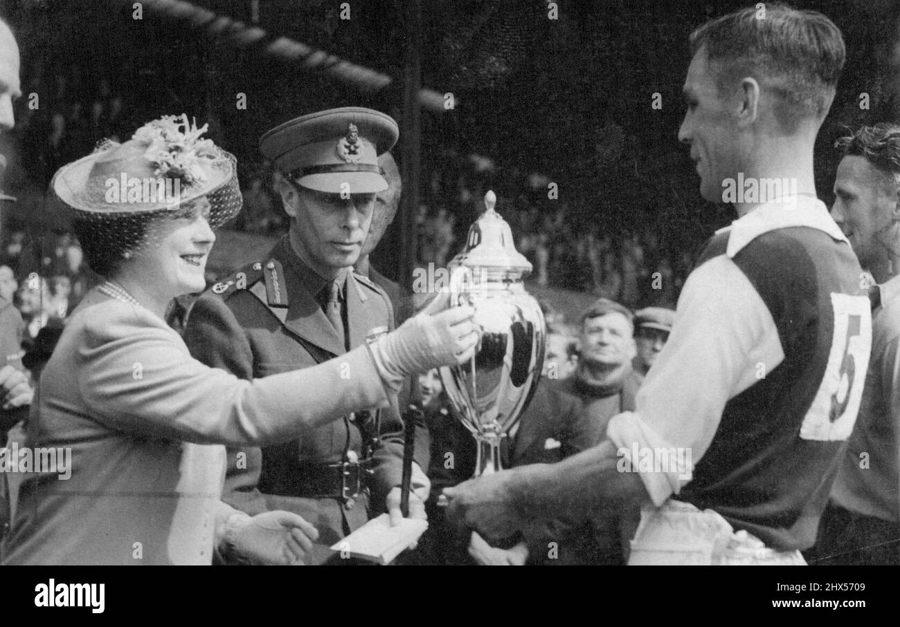 The King and Queen at Football Match - la Regina che presenta la Coppa a Smith Capitano della squadra della Difesa civile. Le loro Majesties, il re e la regina di giorno hanno fatto una visita al ponte di Stamford per guardare la partita di calcio tra l'esercito e la difesa civile (associazione atletica di polizia). Maggio 16, 1942. (Foto di Fox Photos). Foto Stock