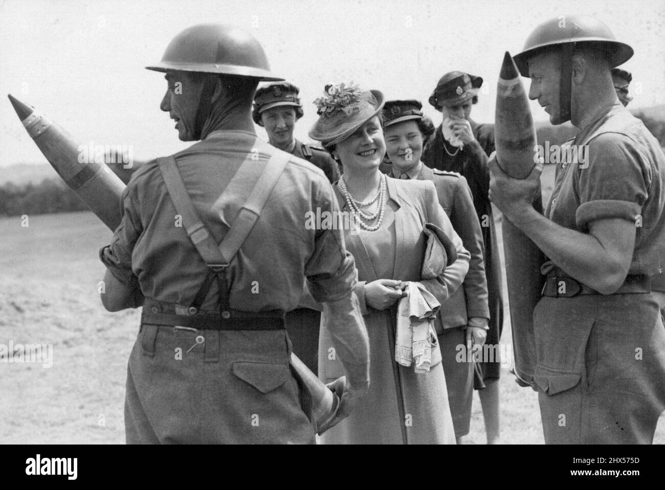 King e Queen Visita A.A. - La regina che guarda i gunner maneggiare 3,7 pollici conchiglie quando ha visitato i siti anti-flying bomba. Ciò che ha catturato l'occhio dei due soldati è fuori dal quadro - ma la regina ha condiviso la barzelletta. Il Re e la Regina, durante una visita alle stazioni di armi A.A. che sono in azione contro le bombe volanti nel sud dell'Inghilterra, vide una bomba volante in parte abbassata da un pilota da caccia e in parte da un fuoco. Luglio 12, 1944. Foto Stock