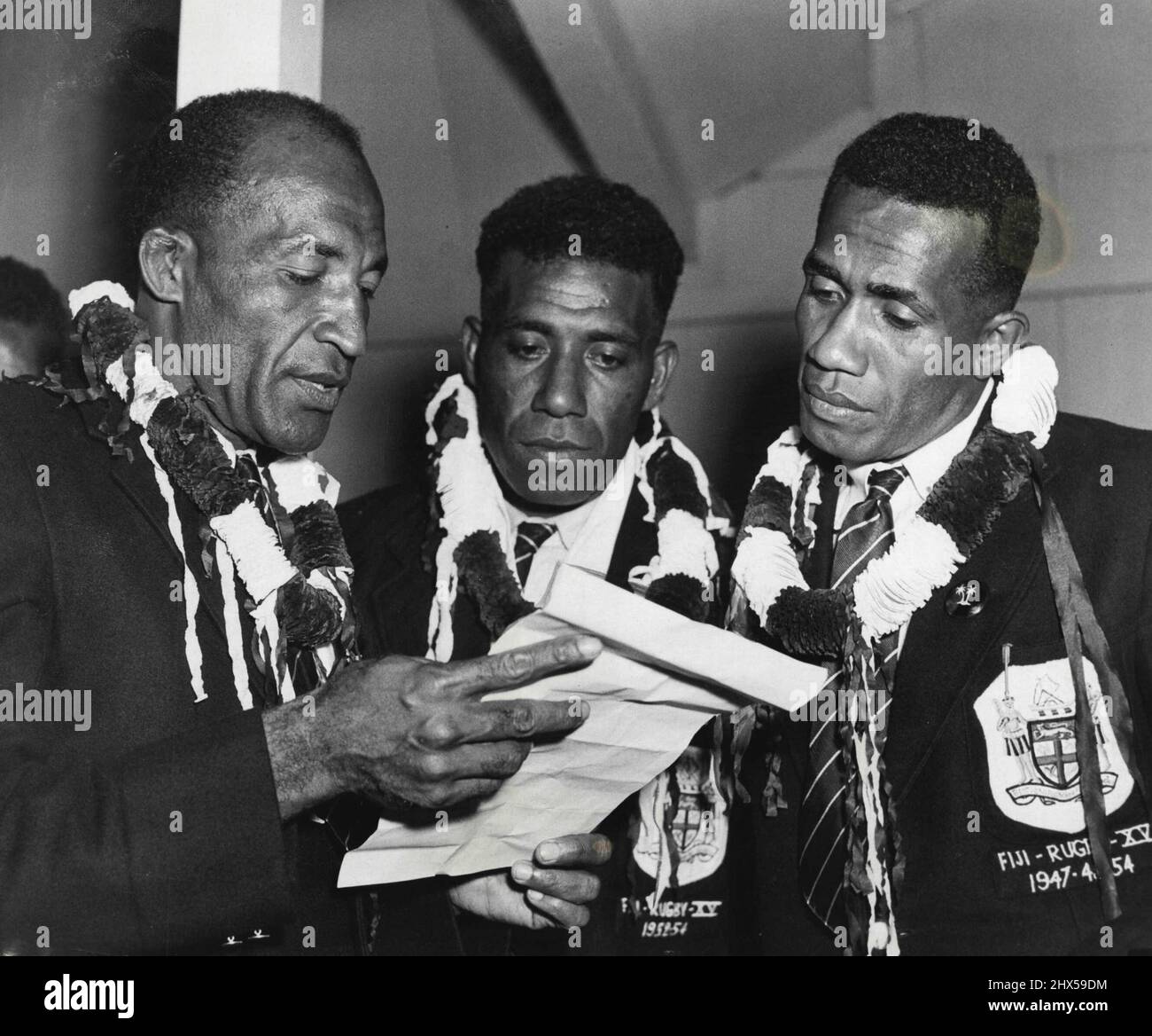 3 membri del Fijian R.U. Squadra. Due membri del team Fijian Rugby Union ascoltano il loro capitano veterano, Apakuki Tuitavua (a sinistra), mentre lui ***** . Maggio 06, 1954. Foto Stock