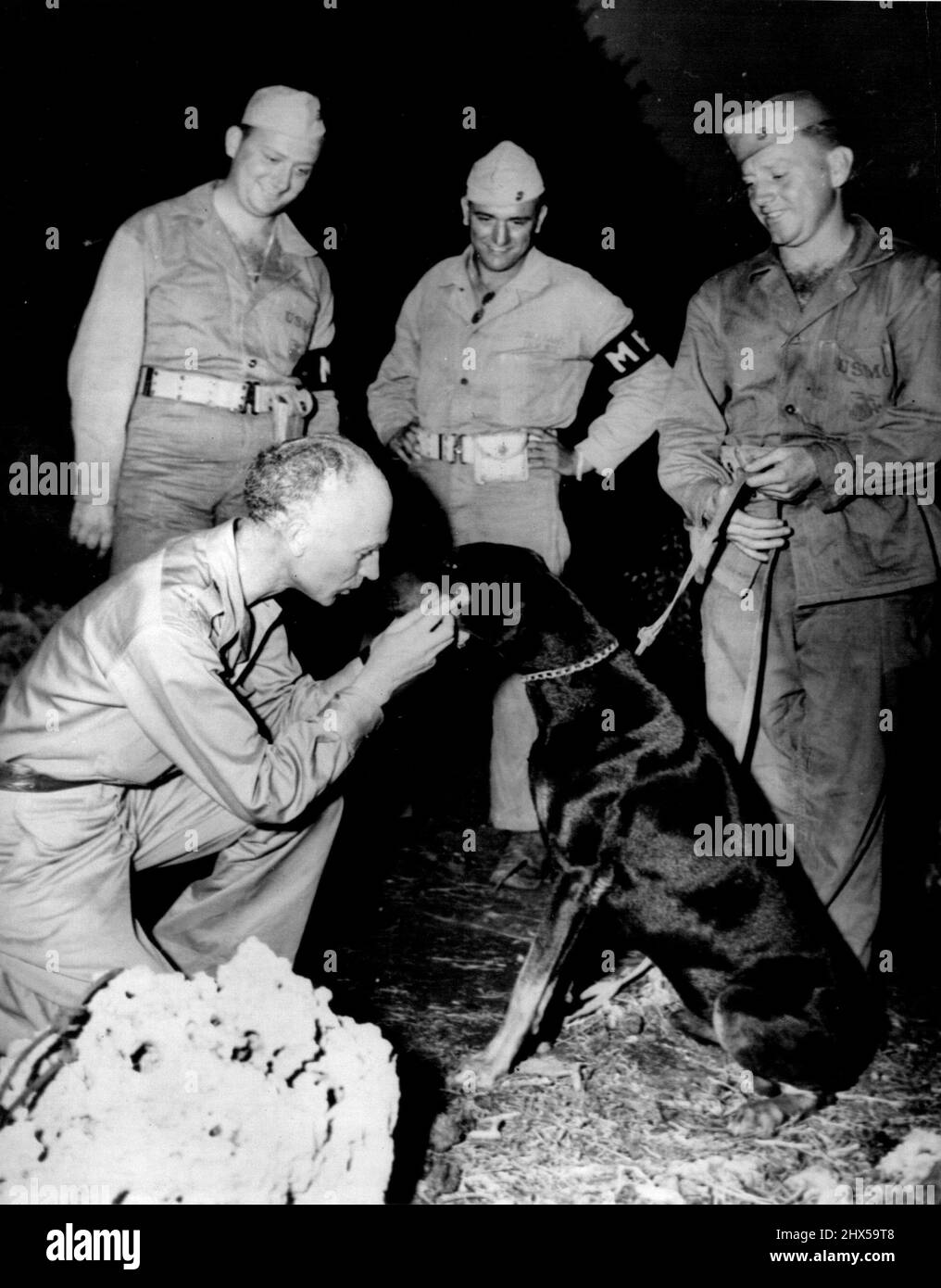Ernie Pyle su New Beat -- Ernie Pyle (a sinistra), corrispondente di guerra che ha recentemente lasciato i campi di battaglia d'Europa per coprire il teatro pacifico della guerra, conosce due tipi di cani del diavolo, 'dove nel Pacifico'. Fu la prima volta che Pyle, celebrato per le sue storie su uomini arruolati dei campi di battaglia, incontrò un cane da guerra marino. Il cane è 'Jeep', un scout e pattugliamento di sicurezza Doberman Pinscher. Si incontrarono mentre 'Jeep' era su un orologio di guardia regolare, vicino al posto di comando del generale maggiore Graves B. Erskine, comandante generale della terza Divisione Marina. Febbraio 9, 1945. (Foto di Official U.S.M Foto Stock