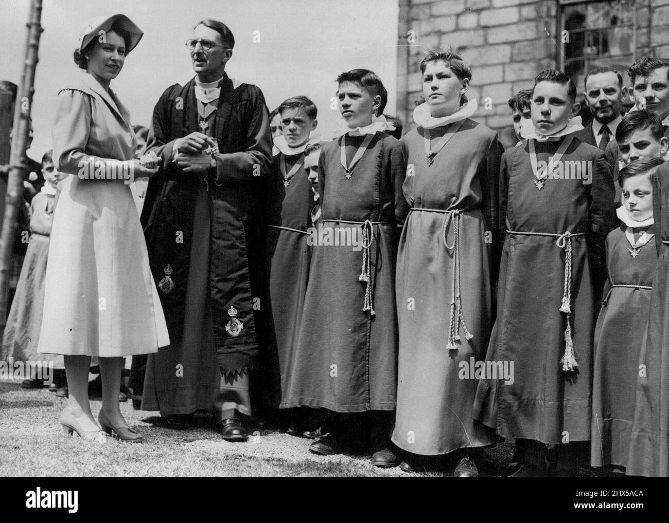 La Regina nel Regno di Scozia - la Regina nel cortile della Canongate Kirk dove piantò un albero di Cerry. La Kirk è la 'Chiesa Parrocchiale' di Holyroodhouse. Con lei è il Reverendo Donald Selby Wright. I coirboys Kirk in cassocks rossi con nastri blu stanno mantenendo uno sguardo stretto davanti. Ieri sua Maestà ha visitato il suo regno scozzese per la prima volta durante il suo regno. Sarà in residenza nel palazzo di Holyroodhouse per i prossimi giorni e ieri ha avuto un ciclo occupato di impegni ufficiali. Giugno 26, 1952. (Foto di Paul Popper). Foto Stock