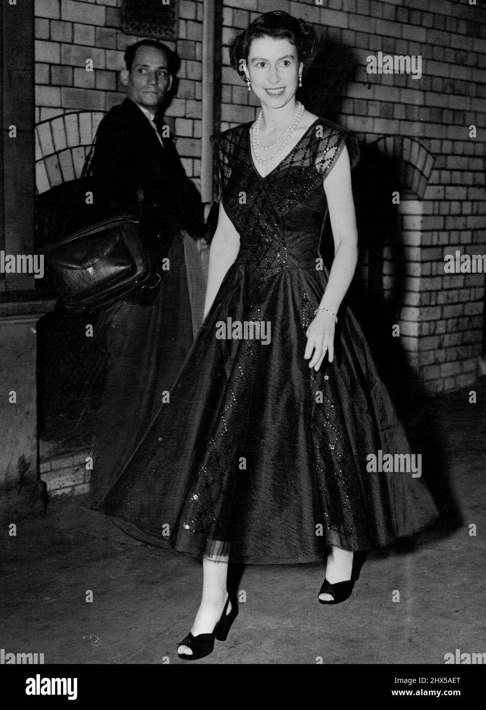 Raggiante in un abito a ballerina in pizzo blu senza maniche, la Regina Elisabetta arriva in una visita a sorpresa al Wyndham's Theatre di Londra per vedere "The Boy Friend". Agosto 11, 1954. (Foto di Daily Mirror). Foto Stock