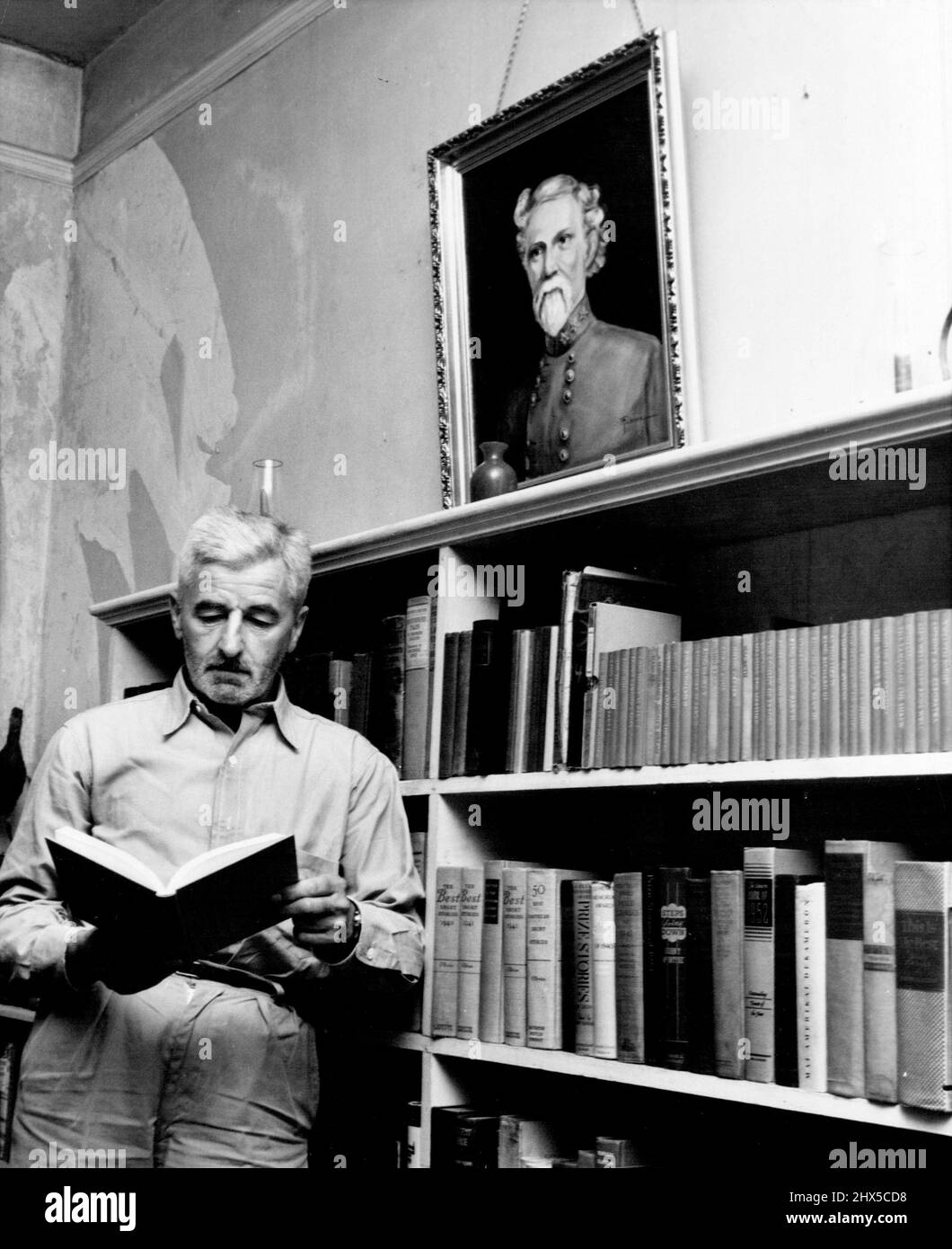 Radici di uno scrittore - William Faulkner legge sotto un dipinto di suo nonno, che era un ufficiale confederato nella guerra civile. La pittura è stata fatta dalla madre di Faulkner, che è ancora viva. Nota la somiglianza familiare tra l'autore e il suo antenato, le tradizioni familiari del Sud svolgono un ruolo importante in molti dei suoi romanzi e storie. Giugno 05, 1955. (Foto di United Press). Foto Stock