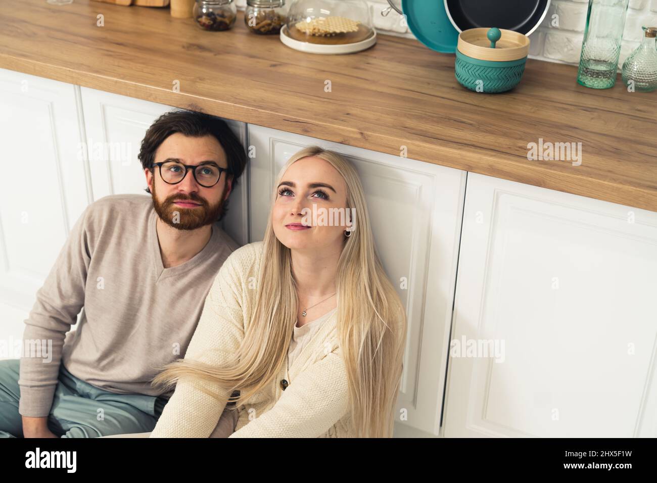 bella coppia caucasica seduta sul pavimento nella cucina moderna e guardando in su, pensando al futuro. Foto di alta qualità Foto Stock