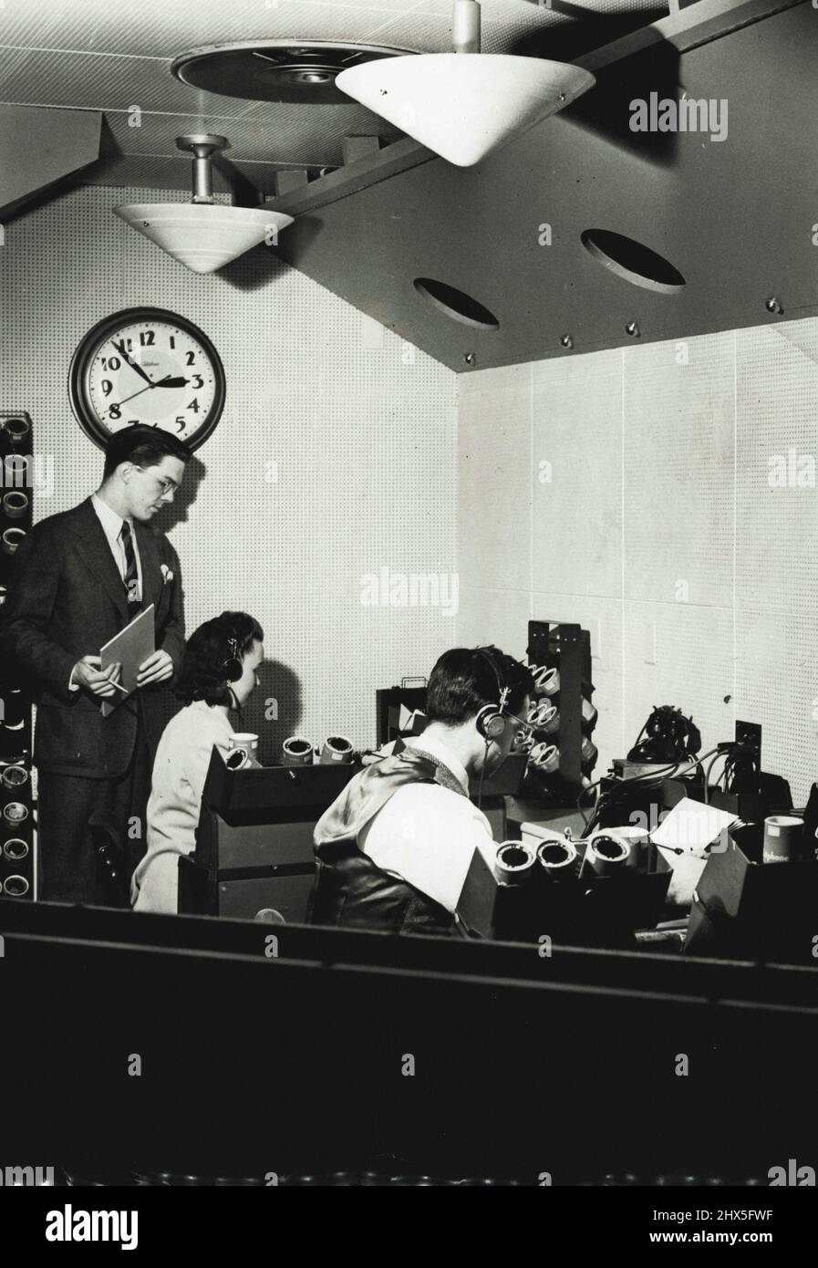Ear to the Ether - Listening Post ... e qui è una vista del CBS ascolto post dall'esterno, guardando attraverso la grande finestra di vetro. Frances Barnard e Benedict Magnes hanno gli auricolari bloccati alla loro testa mentre ascoltano una trasmissione straniera. Può essere da Berlino, Roma, Tokyo o Chungking. Magnes è un esperto in arabo. Traduce anche tedesco, francese, italiano. Miss Barnard ascolta solo le trasmissioni in inglese. Luglio 5, 1942. (Foto di Herbert Scharfman, International News Photos). Foto Stock