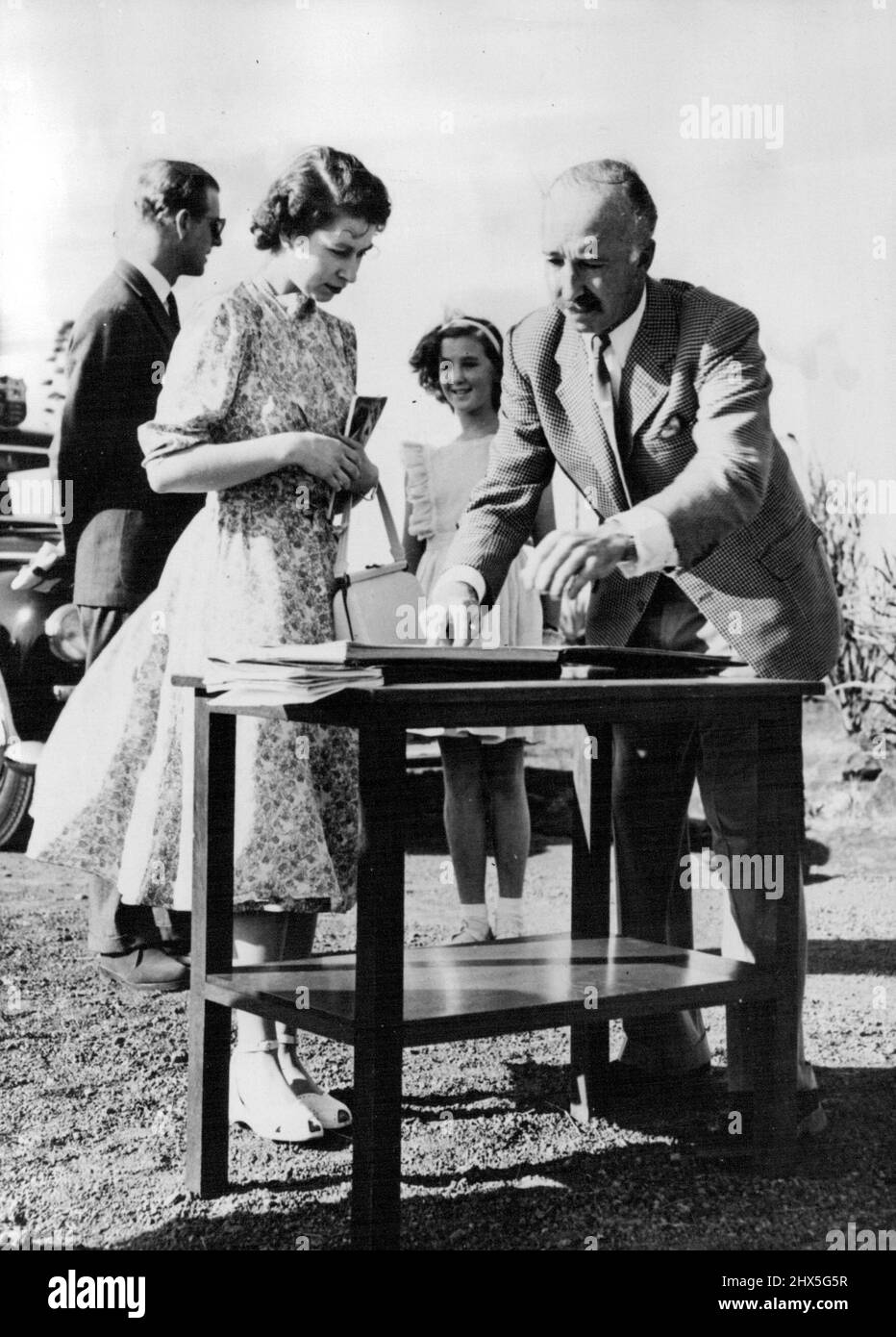 Start Park Tour -- il colonnello Mervyn Covie apre il libro visitatori per la Principessa Elisabetta e il Duca di Edimburgo per firmare come arrivano al Parco Nazionale di Nairobi, 2 febbraio, per iniziare un tour in auto. Il turista reale vide gran parte della vita selvaggia della Presentazione, compreso un leone, a circa 10 metri dalla macchina divorando la sua uccisione. Il Colonnello Cowie è direttore dei Parchi nazionali. Sua figlia, Mitzie, sorride sullo sfondo mentre il Duca chiacchierava con lei. Febbraio 06, 1952. (Foto di stampa associata). Foto Stock