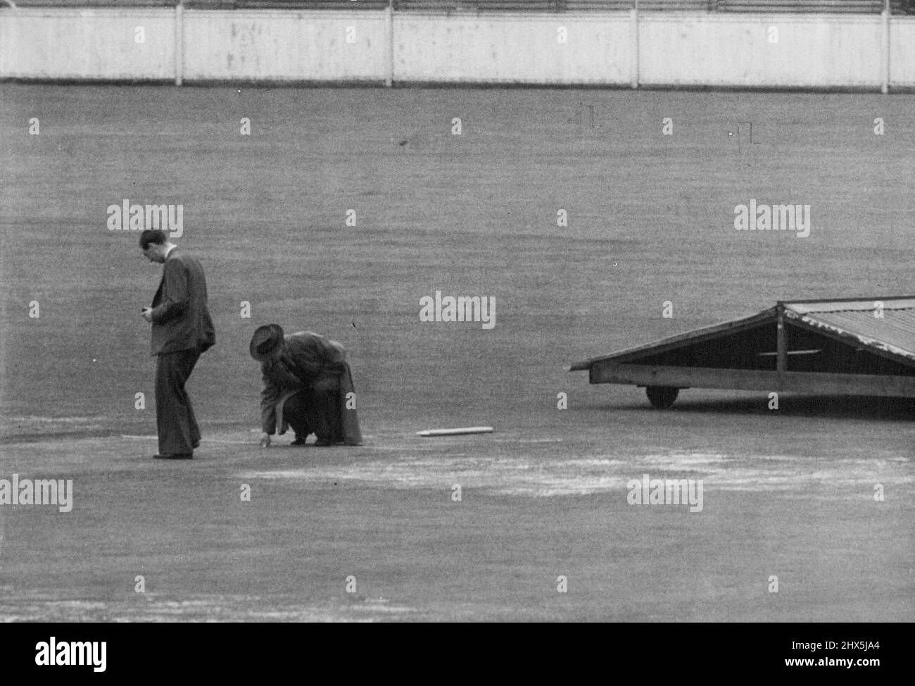 Prova di tutta la notte della folla -- Bradman thumbs il campo e Yardley prova il wicket con il suo piede il wicket con il suo piede all'oval oggi (sab.). Circa 5.000 persone avevano già formato una coda all'Oval entro le 8 di oggi (sabato) per il quinto Test Match. Sotto i cieli grigi formarono due code su entrambi i lati dei tornelli principali. La maggior parte dei tifosi ha cominciato a formarsi appena dopo 5 am molti di cui avevano speso la notte all'aperto. Le prime previsioni, basate su un'ispezione del terreno, erano che la possibilità di giocare prima di pranzo era 'molto remota'. Agosto 14, 1948. (Foto di Reuterphoto). Foto Stock