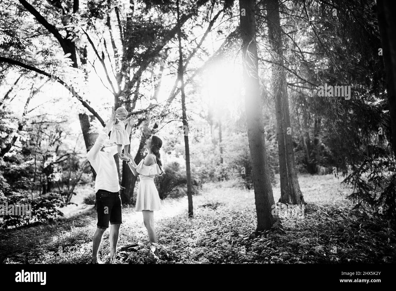 Bella famiglia a piedi al parco, il padre cura ascensore in aria piccola figlia, sorridente, bella bambina stand sulle mani teneri madri, godere felice Foto Stock