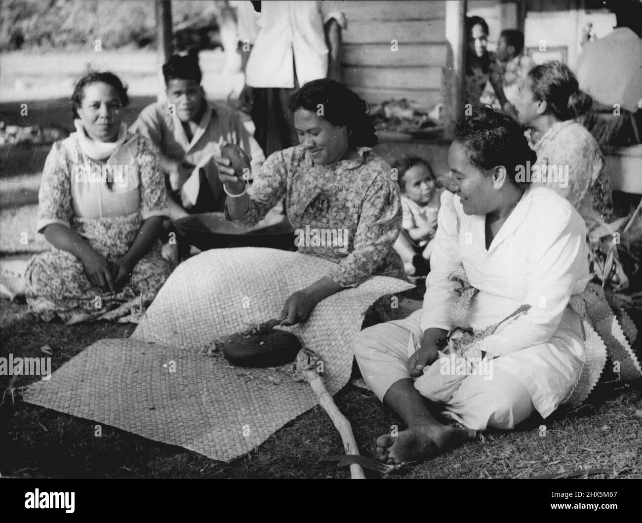 La regina visiterà Tonga -- donna di Tonga che fa Kava. La bevanda nazionale, a base di radici secche di piante appartenenti alla famiglia dei peperoni. A Tonga è la donna che prepara la bevanda, a differenza delle Figi dove gli uomini sono responsabili. La sezione della radice è delimitata tra due pietre di basalto. I frammenti che cadono sul tappeto si spargono sotto. Questi sono riuniti insieme aiuto messo esso la ciotola di legno, visibile sotto il braccio della ragazza. La Regina e il Duca di Edimburgo arriveranno a Tonga il 19 dicembre. La loro seconda sosta nel pacifico. Dicembre 2, 1953. (Foto di Paul Popper). Foto Stock