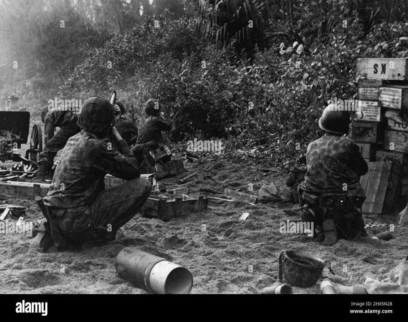 Dietro le linee di Enemy, i Marines combattono... Questa fotografia illustra vividamente l'azione come Marine Saider e Paratroop unità sbarcate su una spiaggia a Bougainville 13 miglia dietro le linee giapponesi per raid un'area di approvvigionamento nemico. Qui sulla spiaggia, ai margini della giungla, Marinez fuoco a cecchini negli alberi che stanno cercando di abbattere la pistola da campo catturata (a sinistra, sfondo) che è stato Yarned contro di loro. Le scatole sulla sabbia contengono munizioni per il 37mm, pezzo di campo. Luglio 16, 1945. (Foto della fotografia ufficiale del corpo Marino degli Stati Uniti). Foto Stock