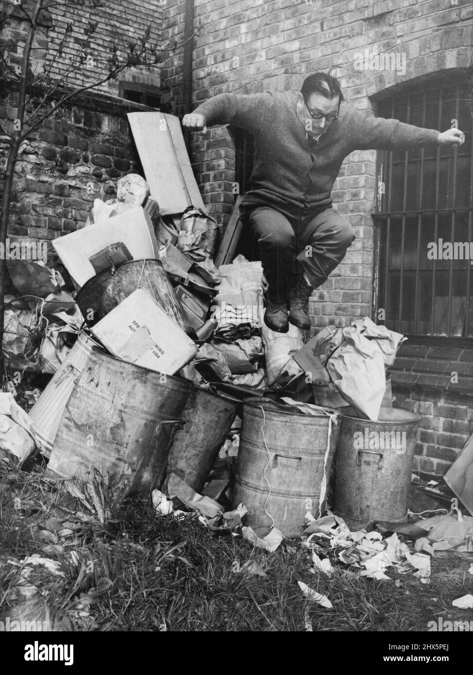 Poiché pesa quasi 15st., Harry Beaver, 42, salterà su e giù all'interno di sette bidoni della spazzatura ogni Mercoledì mattina. E il sig. Lewis Palmer, che tiene un negozio di mobili a Scalford-Road, Melton Mowbray, Leics, gli pagherà 10s. Una settimana per farlo. Il lavoro di Harry è quello di strimolarsi l'accumulo della settimana di carta di scarto - abbastanza per quattordici bidoni della spazzatura, dice il sig. Palmer - negli unici sette bidoni della spazzatura ha il sig. Palmer. E Harry continuerà a farlo fino a quando il consiglio di Melton non permetterà ai polverieri di svuotare i bidoni della spazzatura dei negozianti gratuitamente, o i negozianti, compreso il sig. Palmer, accosentono pagare il 6d. Un bidone della spazzatura Foto Stock