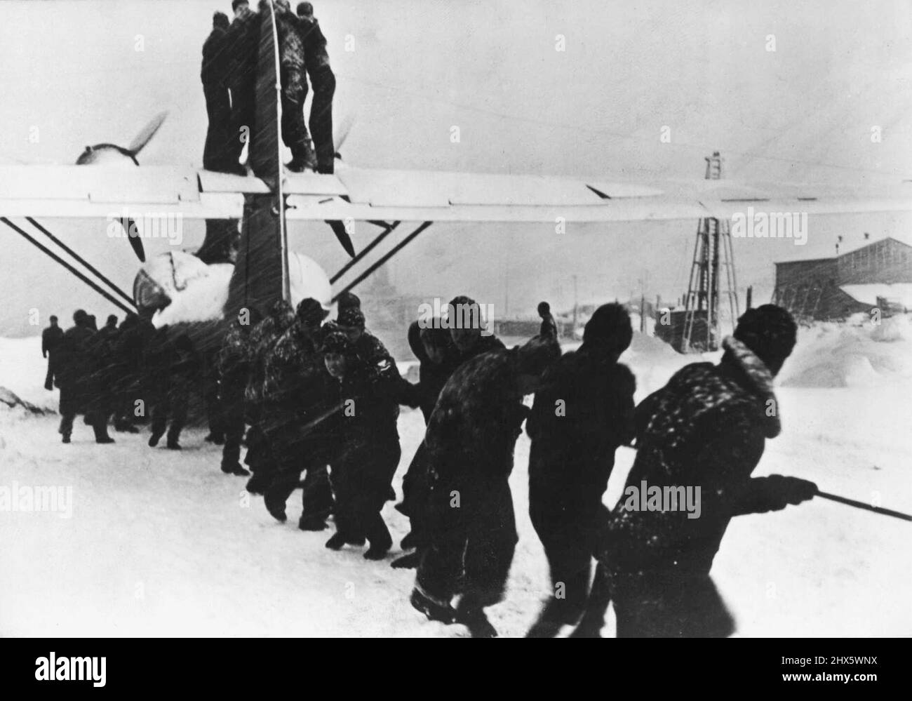 Volantini della Marina degli Stati Uniti negli Aleutiani -- con la neve che frusta i loro volti, uomini di un equipaggio di manutenzione ad una stazione aerea degli Stati Uniti nelle Isole Aleutiche trasportano una barca PBY dalla neve sgocciolata in posizione per il volo. I volantini navy prendono regolarmente i loro grandi bombardieri di pattuglia aloft, spesso nelle condizioni più difficili, per colpire la spedizione e le installazioni giapponesi. Novembre 25, 1954. (Foto di U.S. Office of War Information Picture). Foto Stock