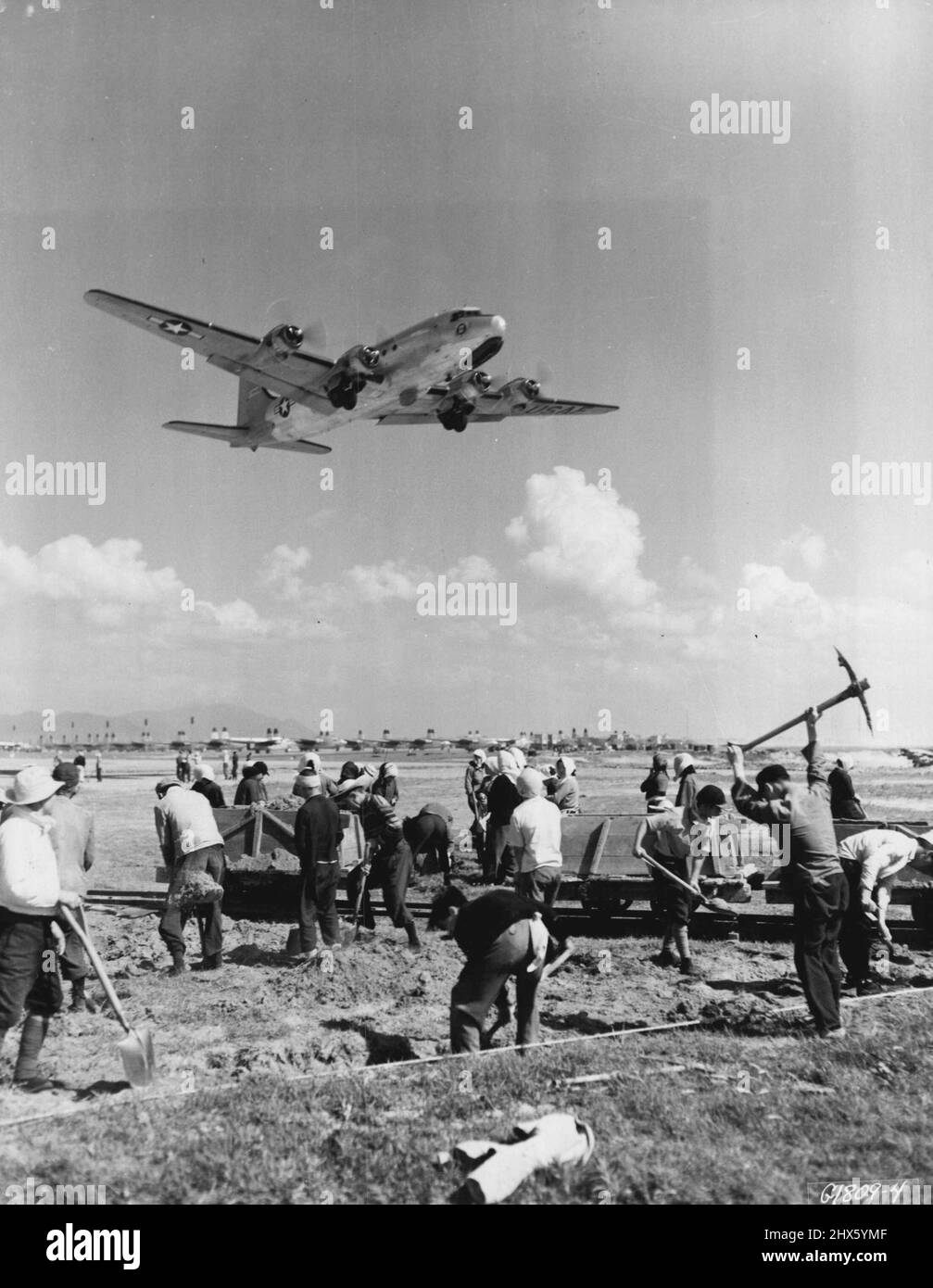 Lavoratori apatetici -- una base aerea in Giappone-come un enorme C-54 Skymaster della Divisione aerea 315th (Cargo di combattimento) ruggisce in testa, lavoratori giapponesi continuano con il loro lavoro di costruzione di pista, completamente ignari del gigante che trasporta il carico sopra loro. La vista degli aerei dell'Estremo Oriente che decollano e atterrano è diventata così comune che i lavoratori raramente si preoccupano di guardarli. Agosto 9, 1951. (Foto da U.S. Air Force Photo).;lavoratori Apatetici -- una base aerea in Giappone-come un enorme C-54 Skym Foto Stock