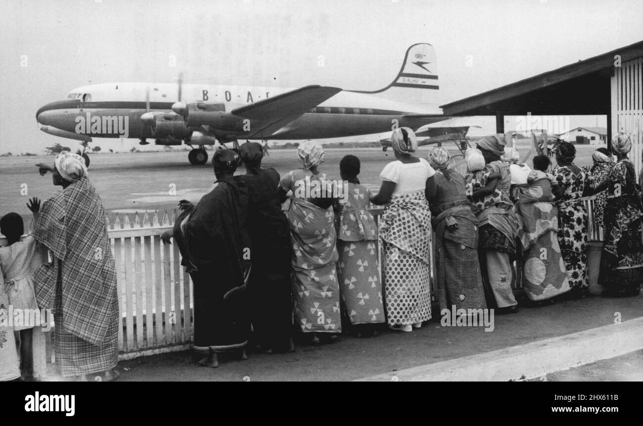 Guardare gli aerei andare da . . . -- l'arrivo e la partenza di aerei internazionali attrae sempre i turisti all'Aeroporto Municipale di Accra. Qui le donne africane, nei loro vestiti variopinti, alcune con i loro bambini arenati sulle spalle, guardano un aereo di linea legato alla casa che lascia l'Africa occidentale britannica per la Gran Bretagna. Luglio 12, 1954. (Foto di Paul Popper Ltd.). ;Guardare gli aerei andare da . . . -- l'arrivo e la partenza di aerei internazionali attrae sempre i turisti ad Accra Foto Stock