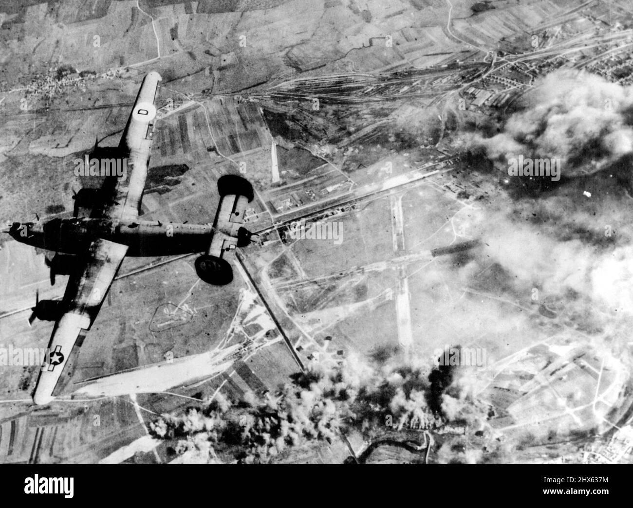 US Planes Blast German Airfield in Francia Un bomber liberatore dell'Ottava forza aerea militare degli Stati Uniti si dirige per la sua base domestica dopo aver contribuito a far esplodere un campo aereo tedesco nei pressi di St. Dizier, in Francia occupata, dove gli edifici amministrativi (in alto a destra) bruciano ferocemente e le bombe esplodono sulla zona dispersa (centro inferiore). Il campo d'aviazione, situato vicino al fiume Marno, è utilizzato dai tedeschi come base difensiva per aerei da combattimento. Nel mese di marzo, 1944 aerei di guerra americani hanno volato 29.016 ferite sopra la Germania e tedesco-h. Foto Stock