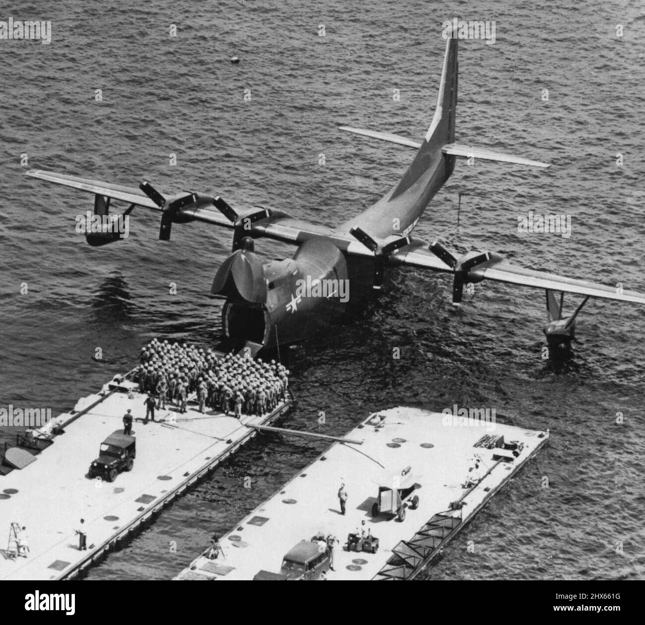 'Flying LST' della Marina -- un gruppo di cento e tre marine di fronte al nuovo idrovolante della Marina, progettato per aprire il suo naso enorme e disgorgere uomini o macchine direttamente su una spiaggia in guerra anfibia. Questa prova preliminare del 'Flying LST' è stato fatto ad un molo galleggiante nella Baia di San Diego, ma la Marina dice l'aereo -- il R3Y-2 -- più tardi metterà gli uomini direttamente a terra su spiagge sabbiose. Agosto 18, 1954. (Foto di AP Wirephoto). Foto Stock