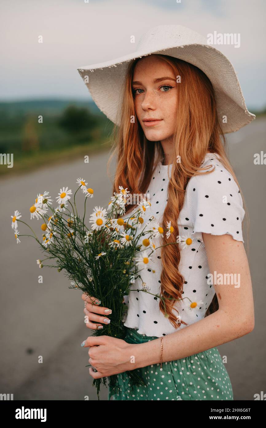 Donna caucasica dai capelli rossi in cappello posa all'aperto mentre tiene  bouquet di fiori e guarda la macchina fotografica. Splendido ritratto per  un design di stile Foto stock - Alamy