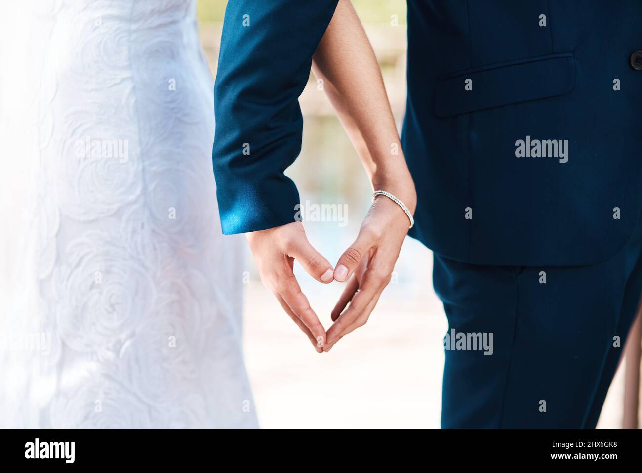 Le ceneri mi hanno fatto la sua metà migliore. Scatto corto di una coppia newlywed irriconoscibile che fa una figura del cuore con le loro mani mentre si levano in piedi all'aperto sul loro Foto Stock