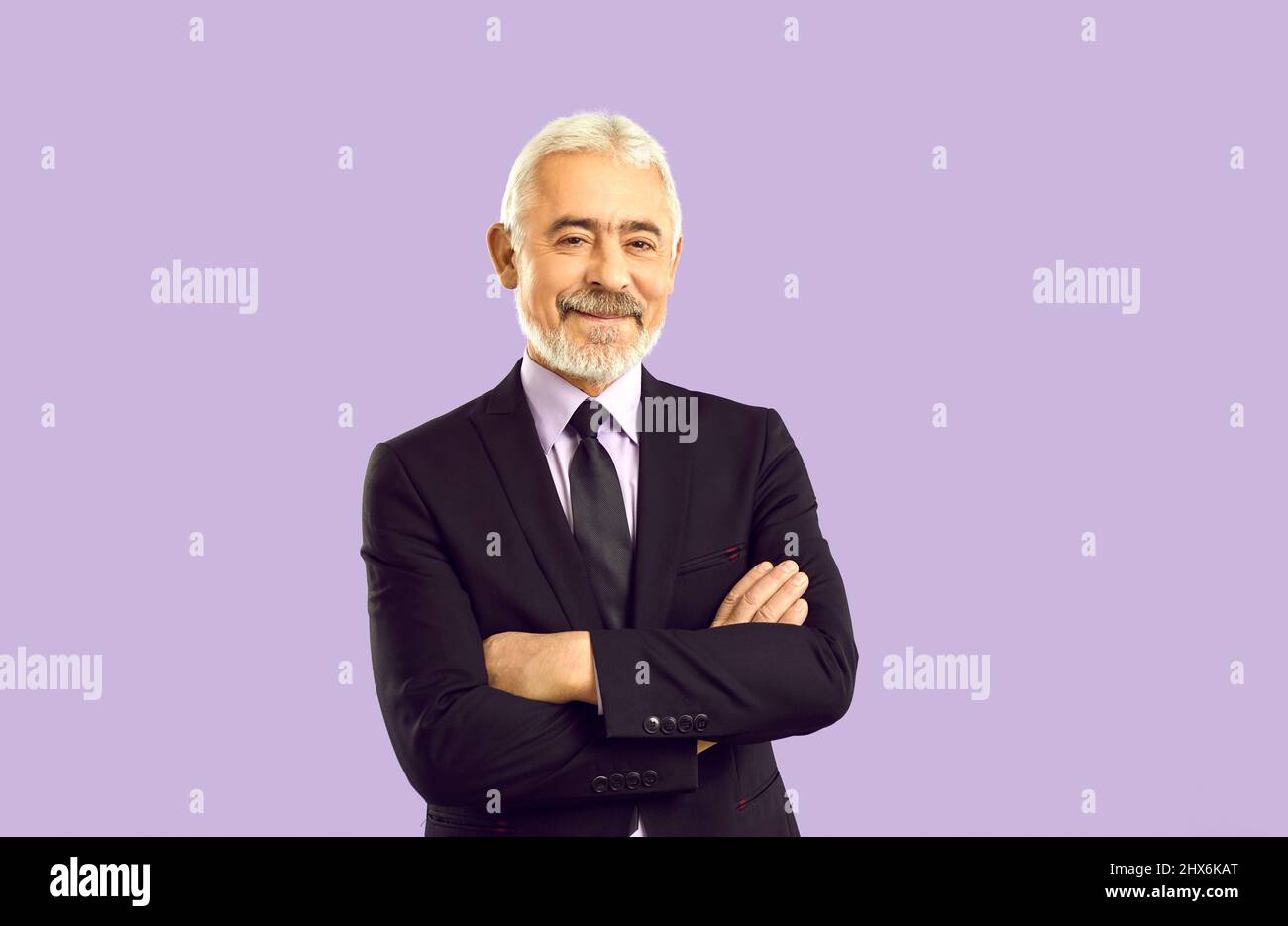 Ritratto di uomo d'affari anziano felice in tuta in piedi su sfondo viola studio Foto Stock