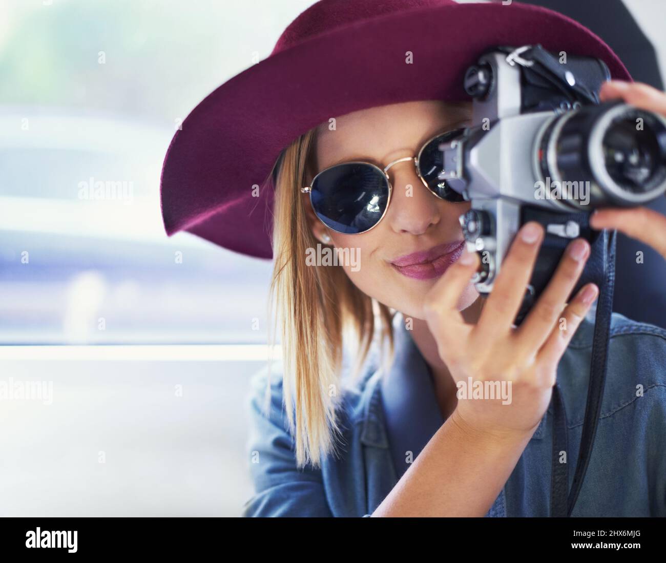 Scattare foto per tutta la vita. Una giovane donna che indossa un cappello e occhiali da sole scattando foto da un'auto. Foto Stock