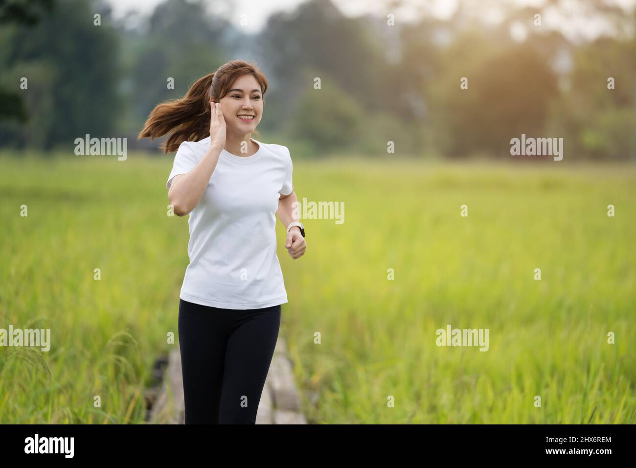 giovane donna che ascolta musica sulle cuffie mentre corre su un sentiero di legno nel campo Foto Stock